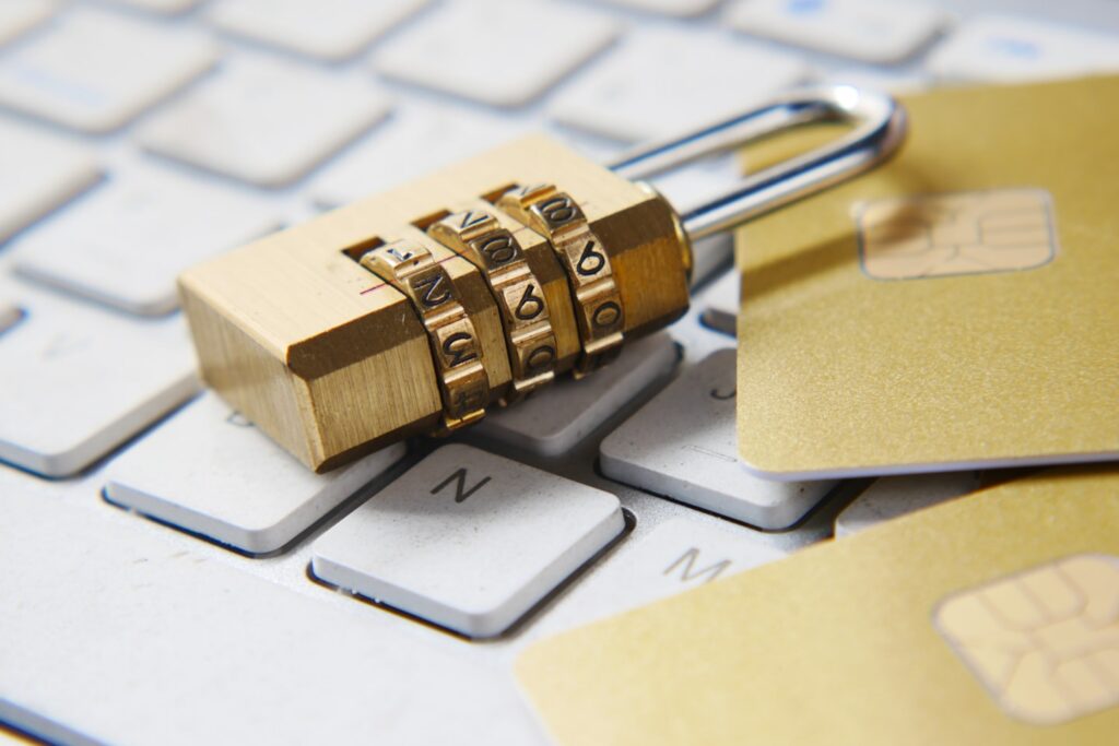 Ein Vorhängeschloss aus Messing mit Zahlenkombination liegt zusammen mit Kreditkarten auf einer Computer-Tastatur als Symbol für Datensicherheit.
